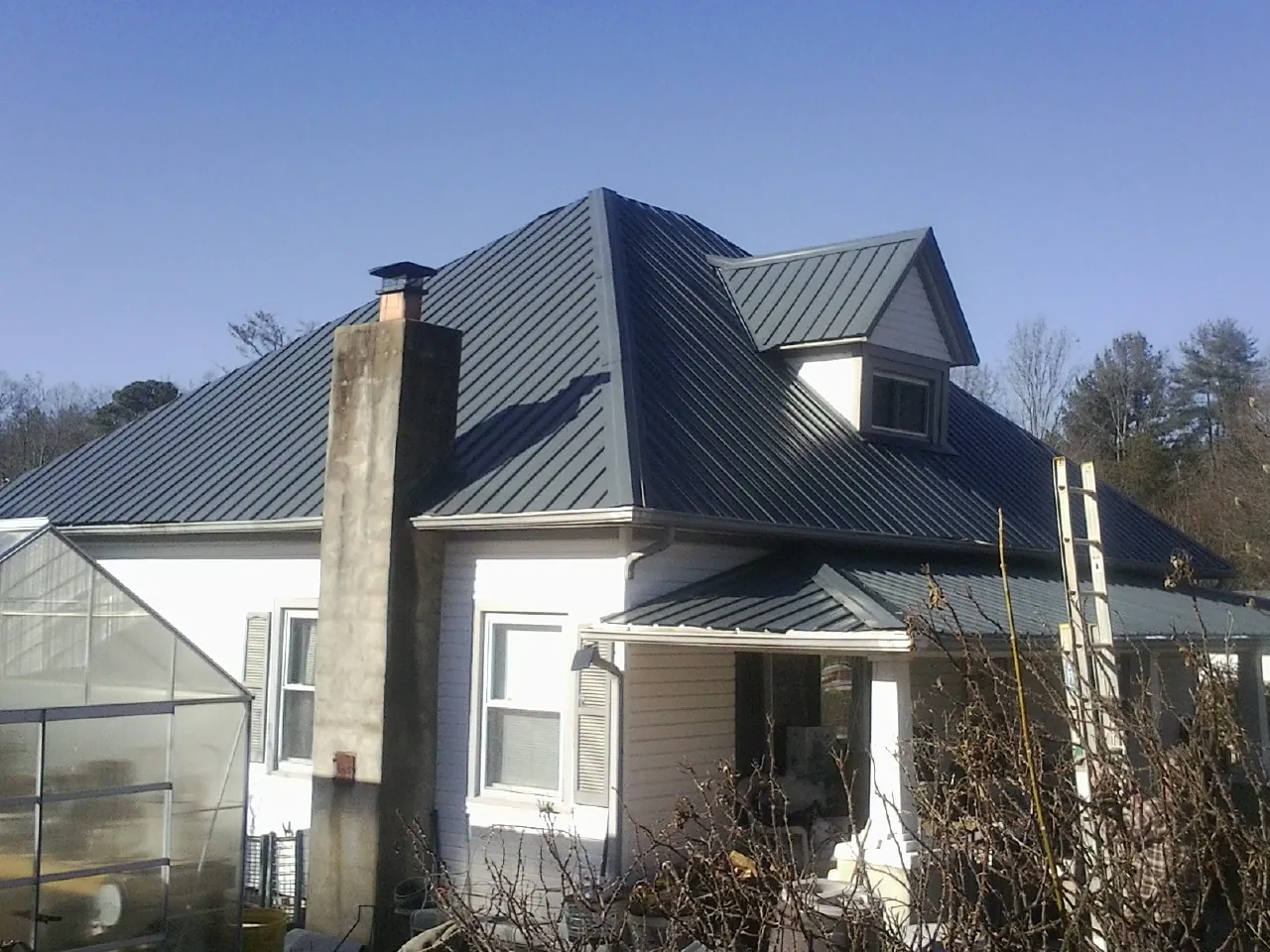 Dark blue standing seam metal roof on a white farmhouse with dormer — Slate & Tile Roof Repair by Roofing Brothers in Kountze