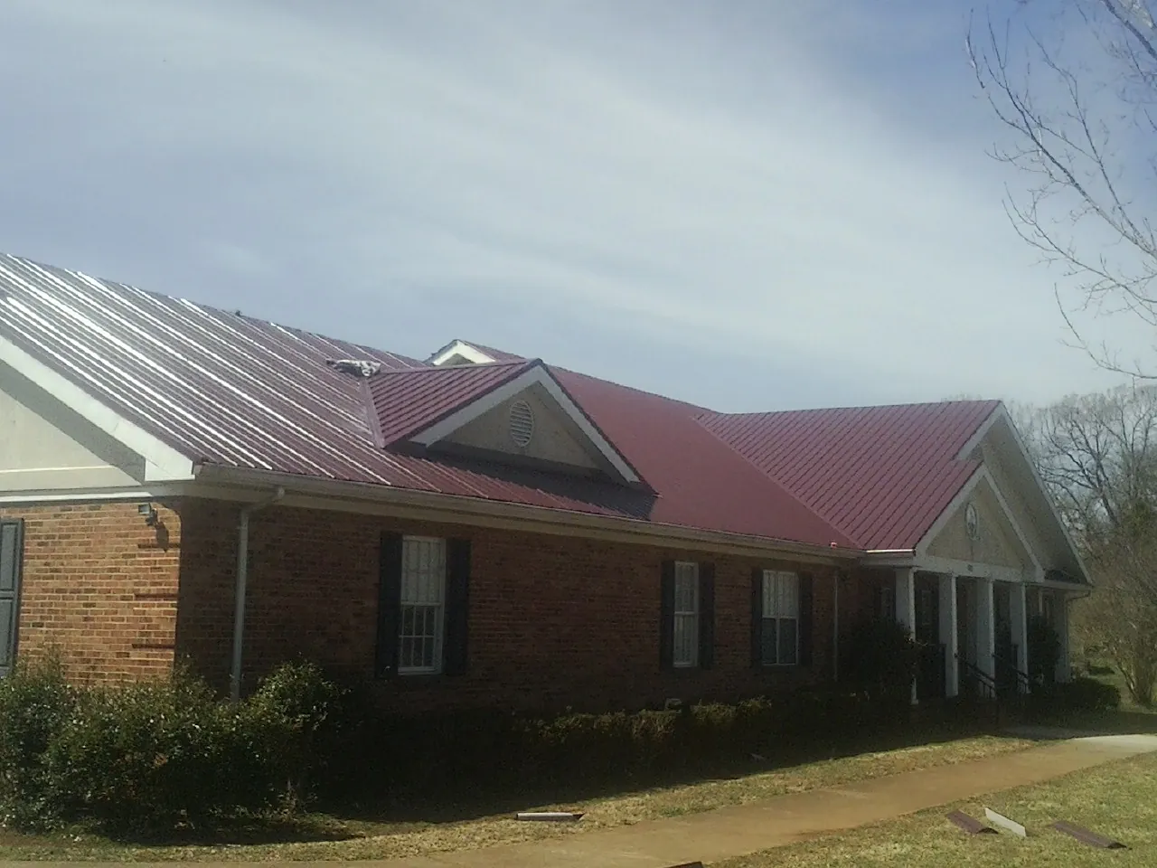 Red metal roof with gabled entries on a long brick building, from a Hail Damage Roof Repair job in Kountze