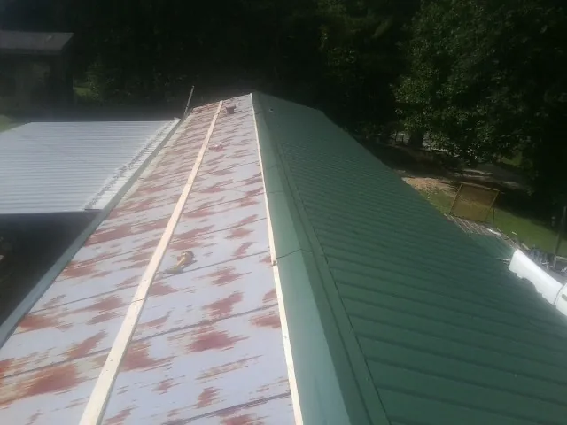 Old rusted panels beside newly installed green metal roofing — Wind Damage Roof Repair by Roofing Brothers in Kountze