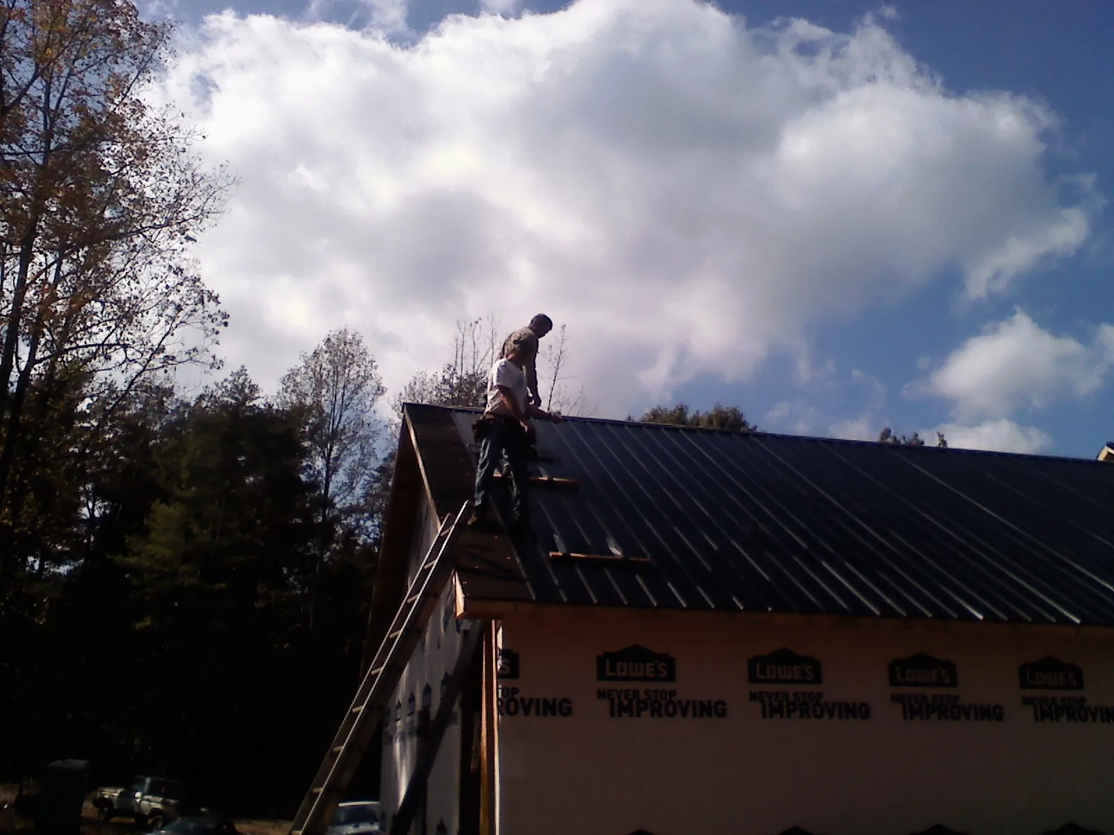 Roofer fastening dark metal panels high against a cloudy sky, from a Roof Inspection job in Kountze