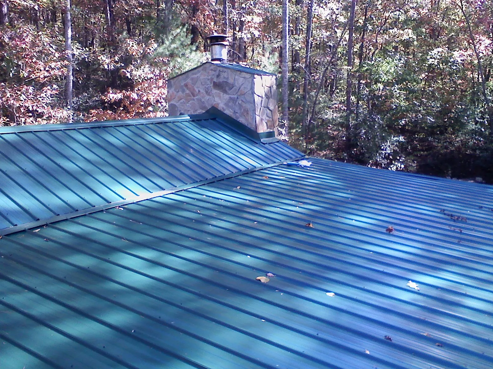 New green metal roof and stone chimney surrounded by autumn woods in Kountze