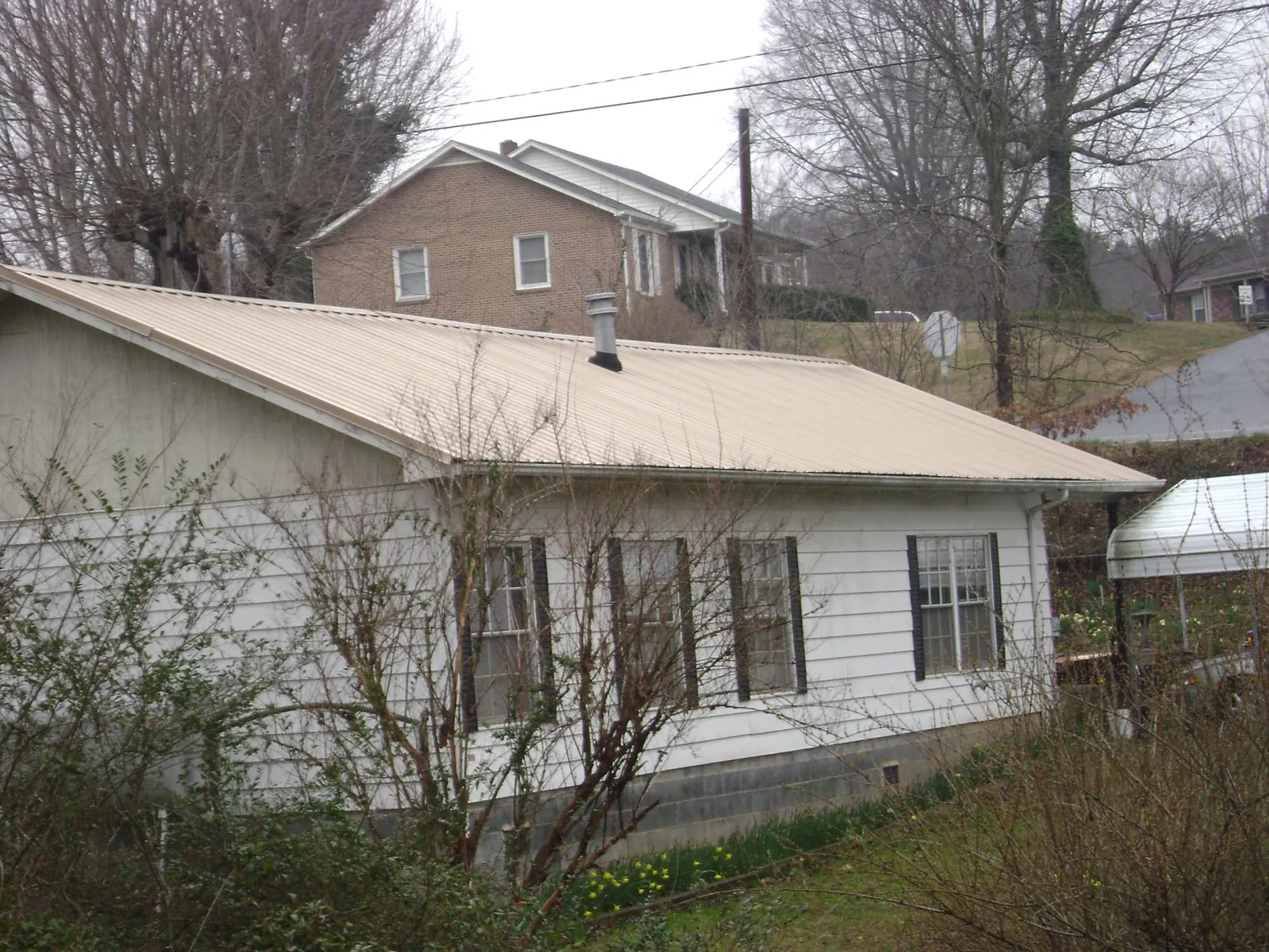 Tan metal roof on a white sided house set into a hillside — Commercial Roofing by Roofing Brothers in Kountze