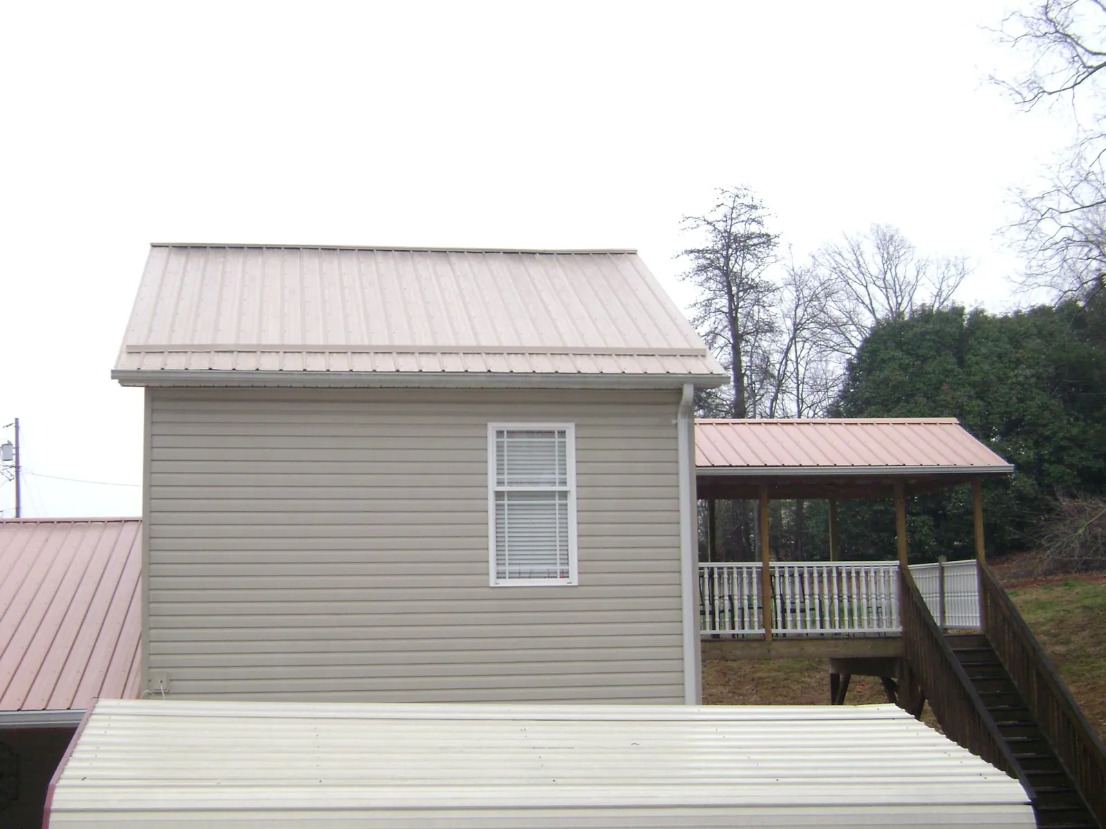 Tan metal roofs on a two story addition and attached porch, from a Roof Replacement job in Kountze